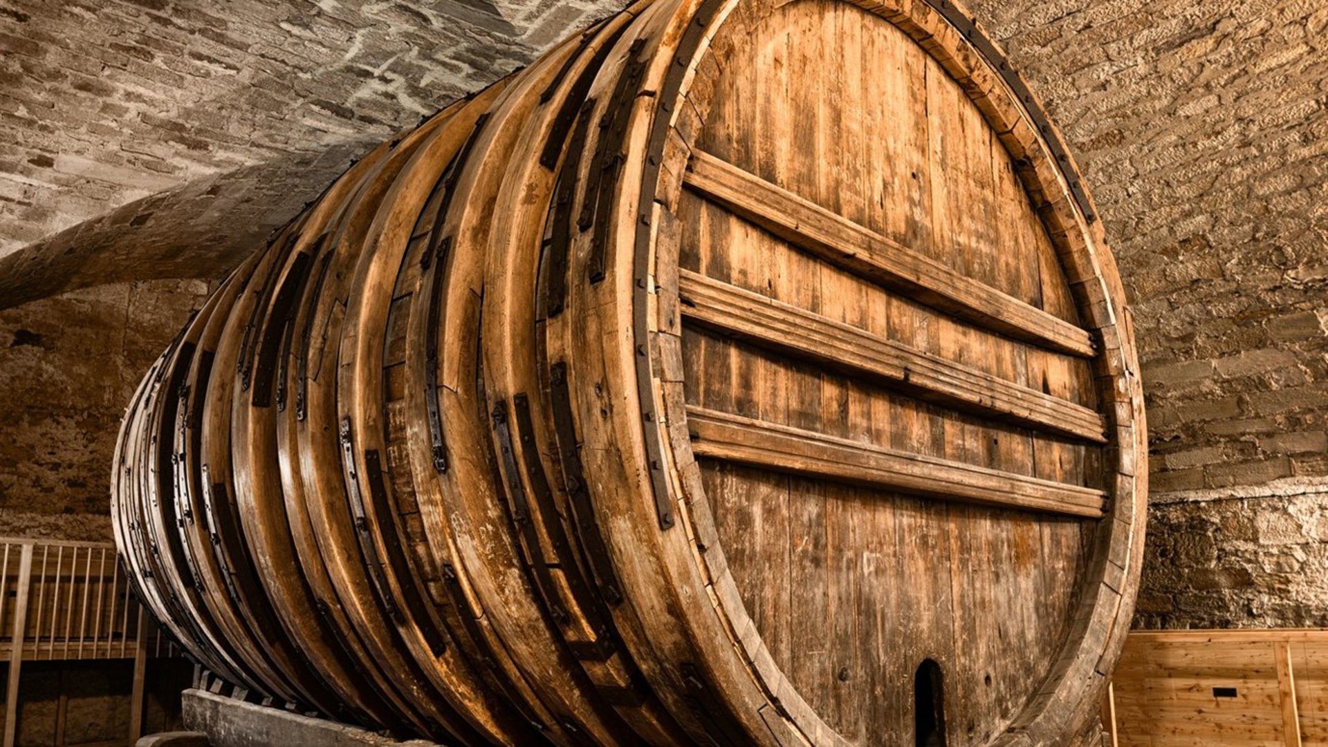 Three quarter view of a giant wine barrel in a vaulted cellar, jacked up upon wooden beams