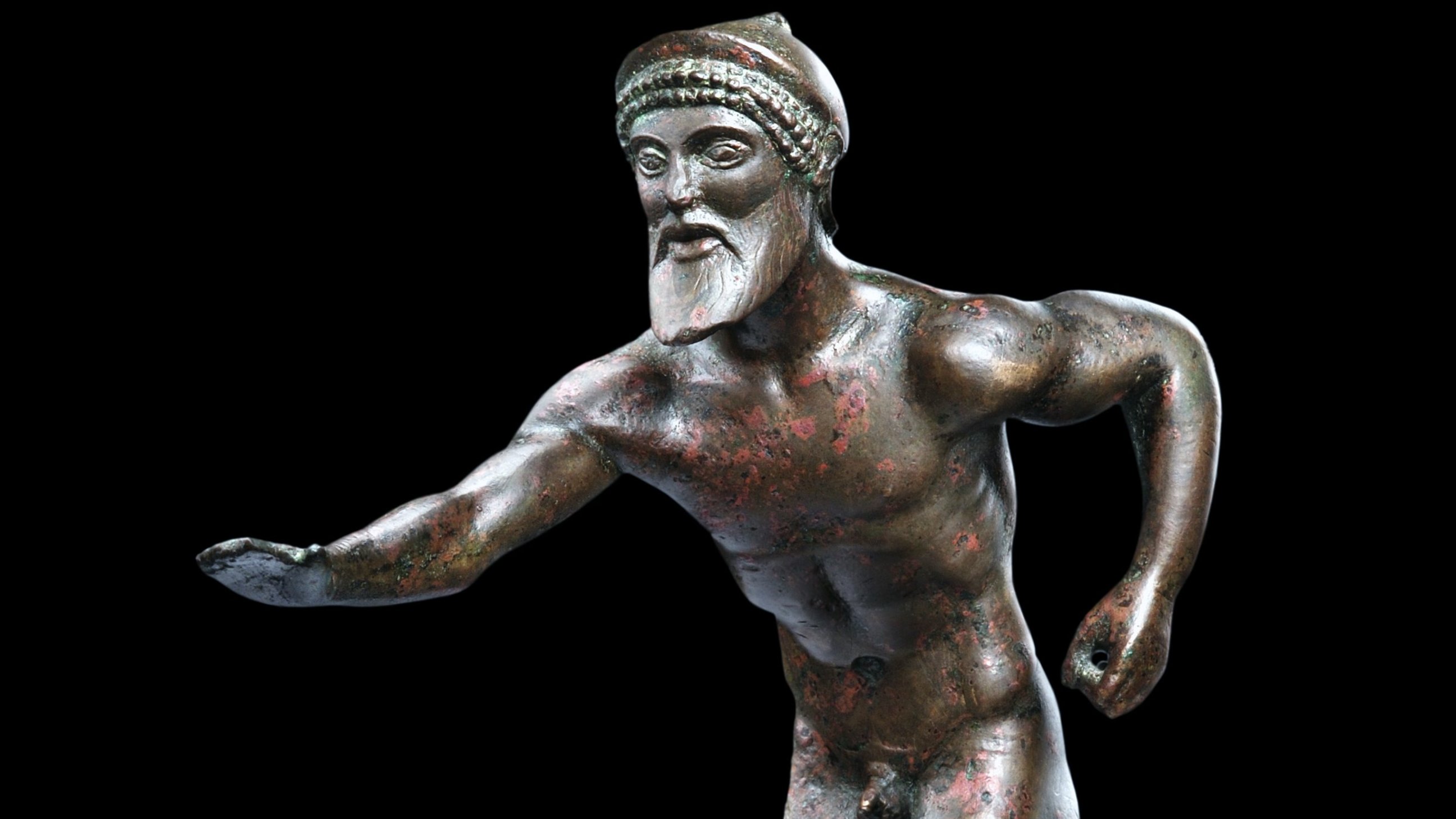 Detail of a bearded male bronze figurine from the hip upwards; one arm is stretched out, the other angled to the back, as if the takes of running; against black background