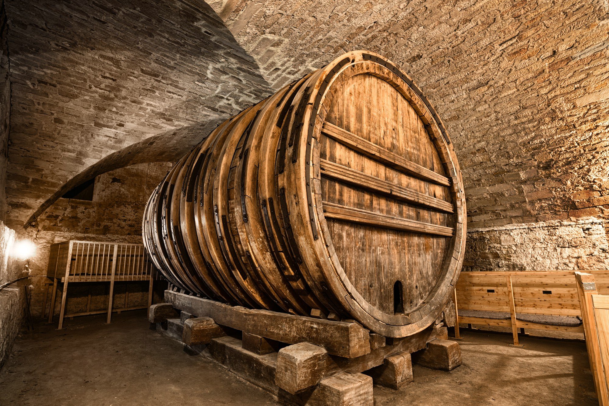 Three quarter view of a giant wine barrel in a vaulted cellar, jacked up upon wooden beams