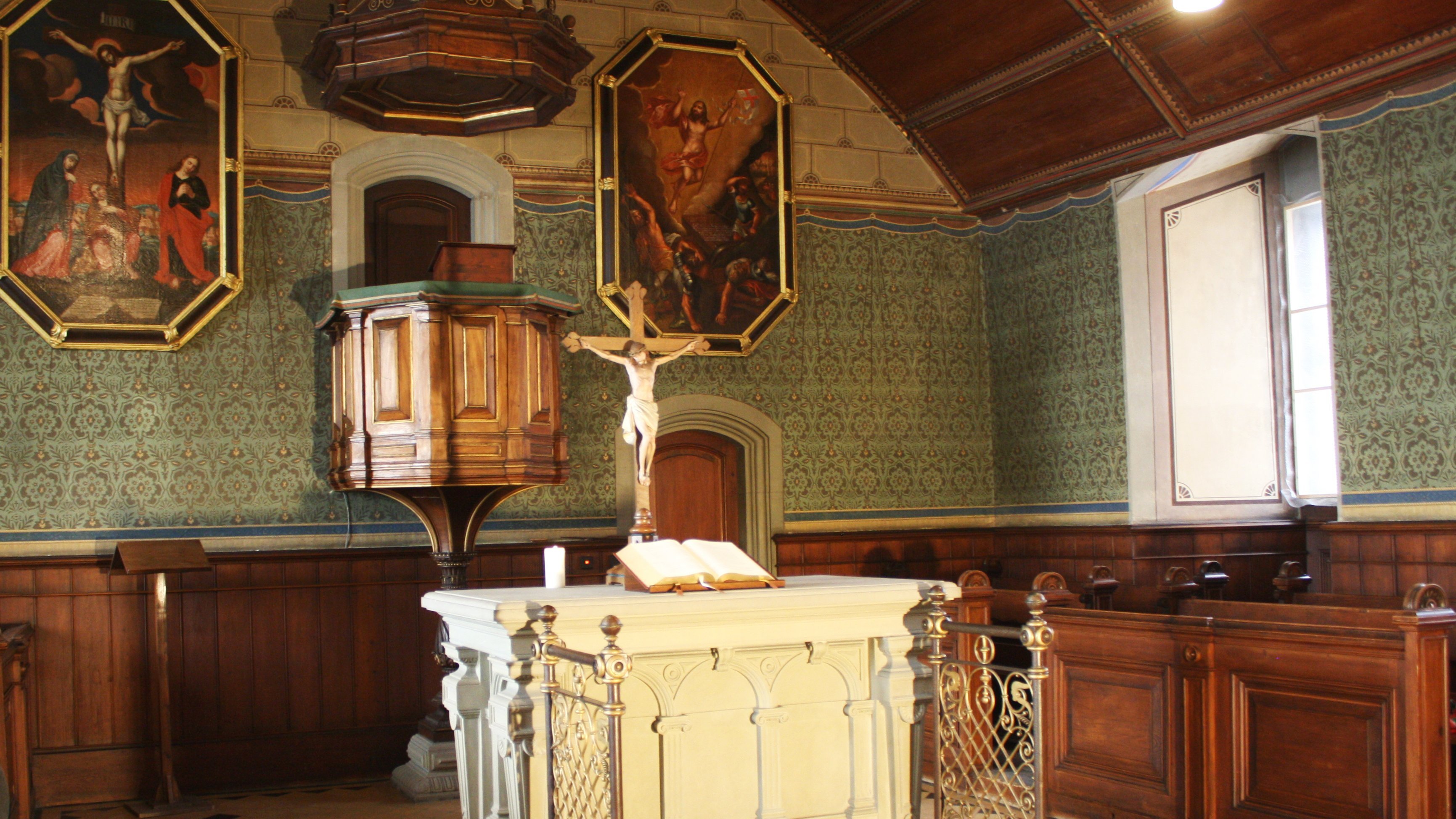 Blick in den Altarbereich der Schlosskirche mit weißem Altar mit aufgeschlagener Bibel, gekreuzigter Christusfigur und hinaufführender Treppe, im Hintergrund Kanzel, flankiert von Malereien des gekreuzigten (links) und in den Himmel fahrenen Christus (rechts)