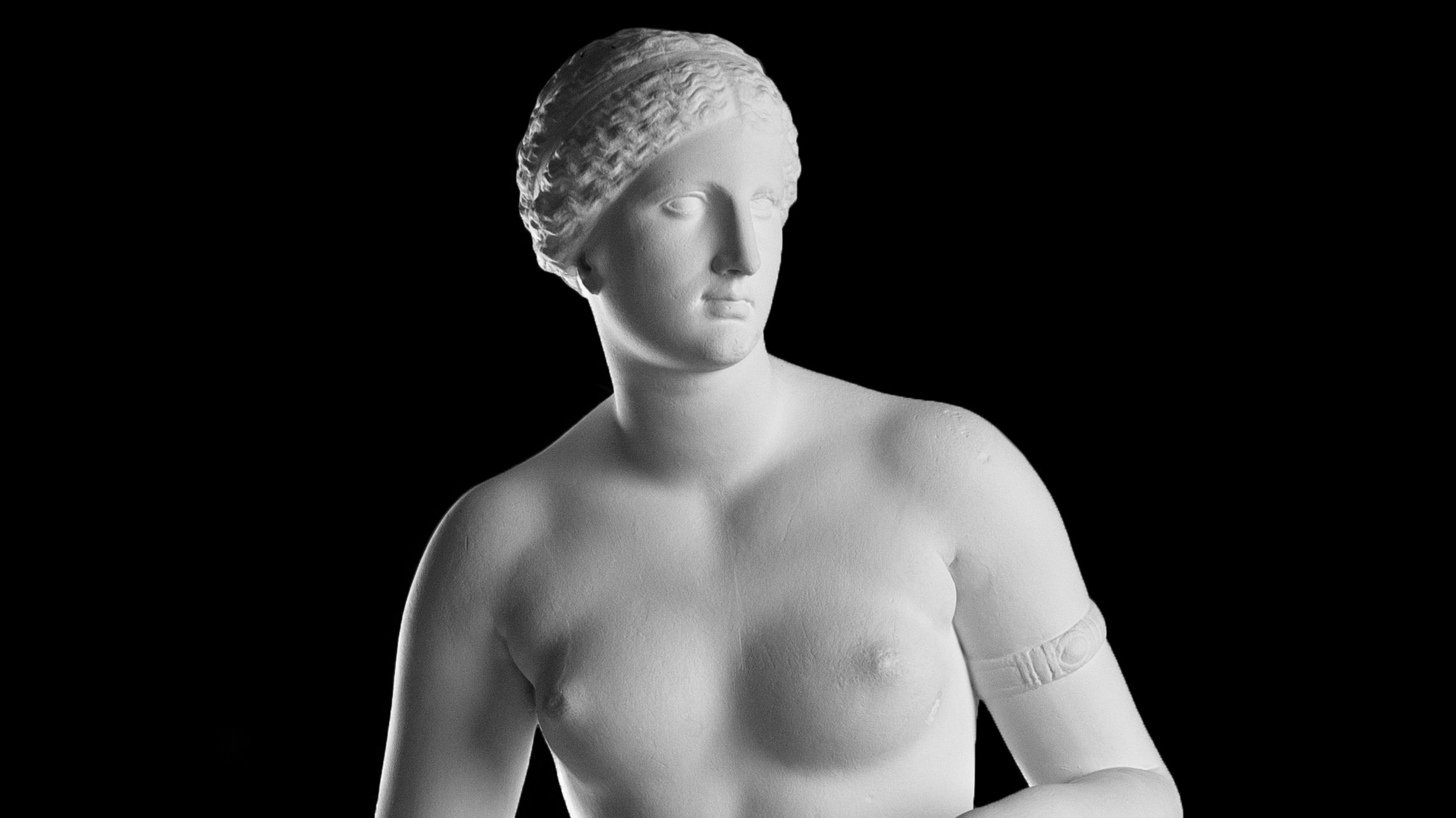 Büsten-Ausschnitt einer weißen Statue einer unbekleideten Aphrodite mit nach rechts geneigtem Kopf und einem Reifen an ihrem linken Arm