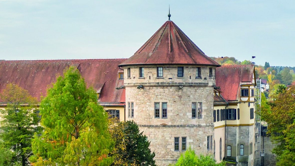 Im Hochformat wird die Westbastion von Schloss Hohentübingen mit weißen Mauern und roten Dächern in spätsommerlicher Begrünung gezeigt.