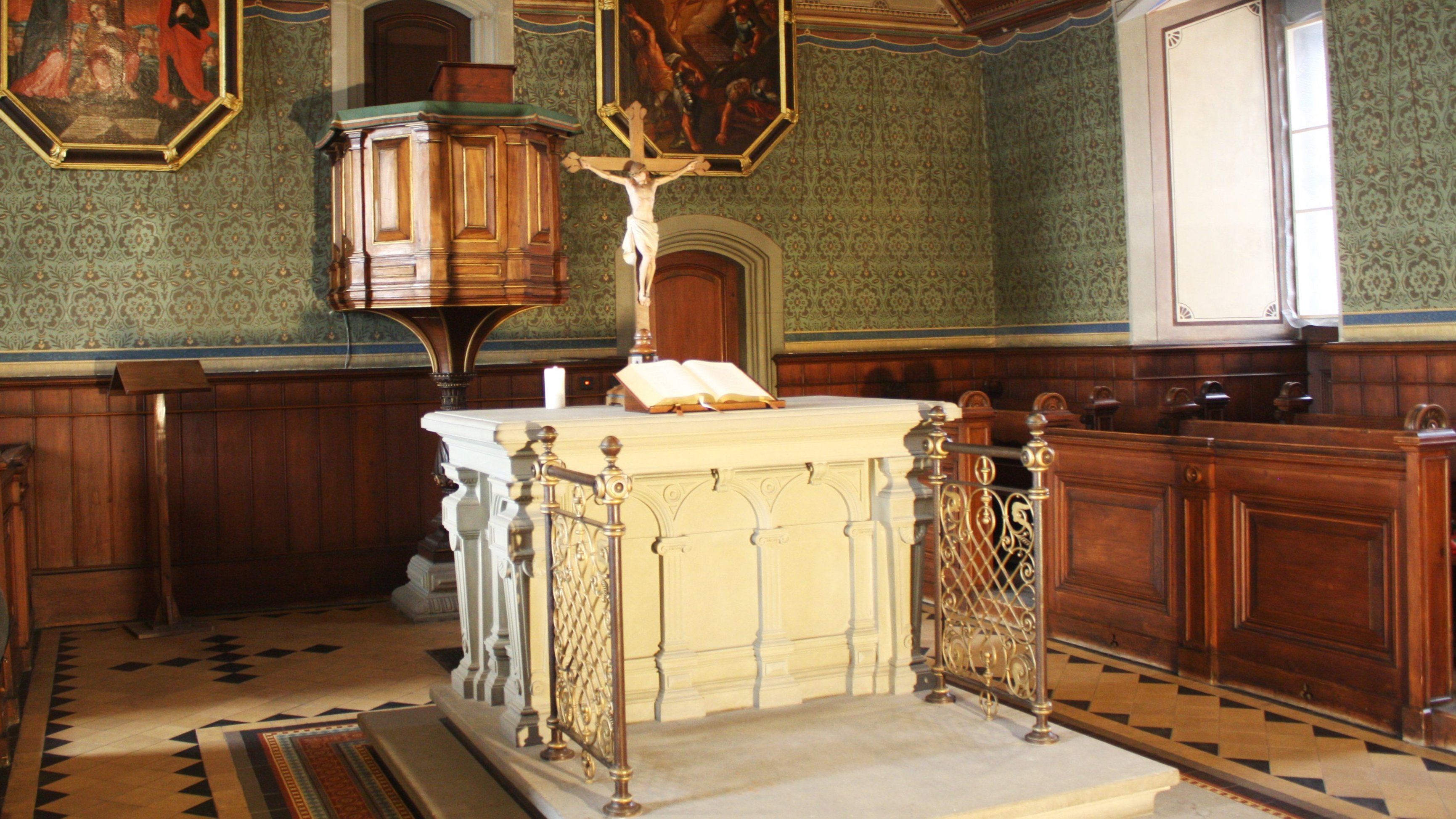 Blick in den Altarbereich der Schlosskirche mit weißem Altar mit aufgeschlagener Bibel, gekreuzigter Christusfigur und hinaufführender Treppe, im Hintergrund Kanzel, flankiert von Malereien des gekreuzigten (links) und in den Himmel fahrenen Christus (rechts)