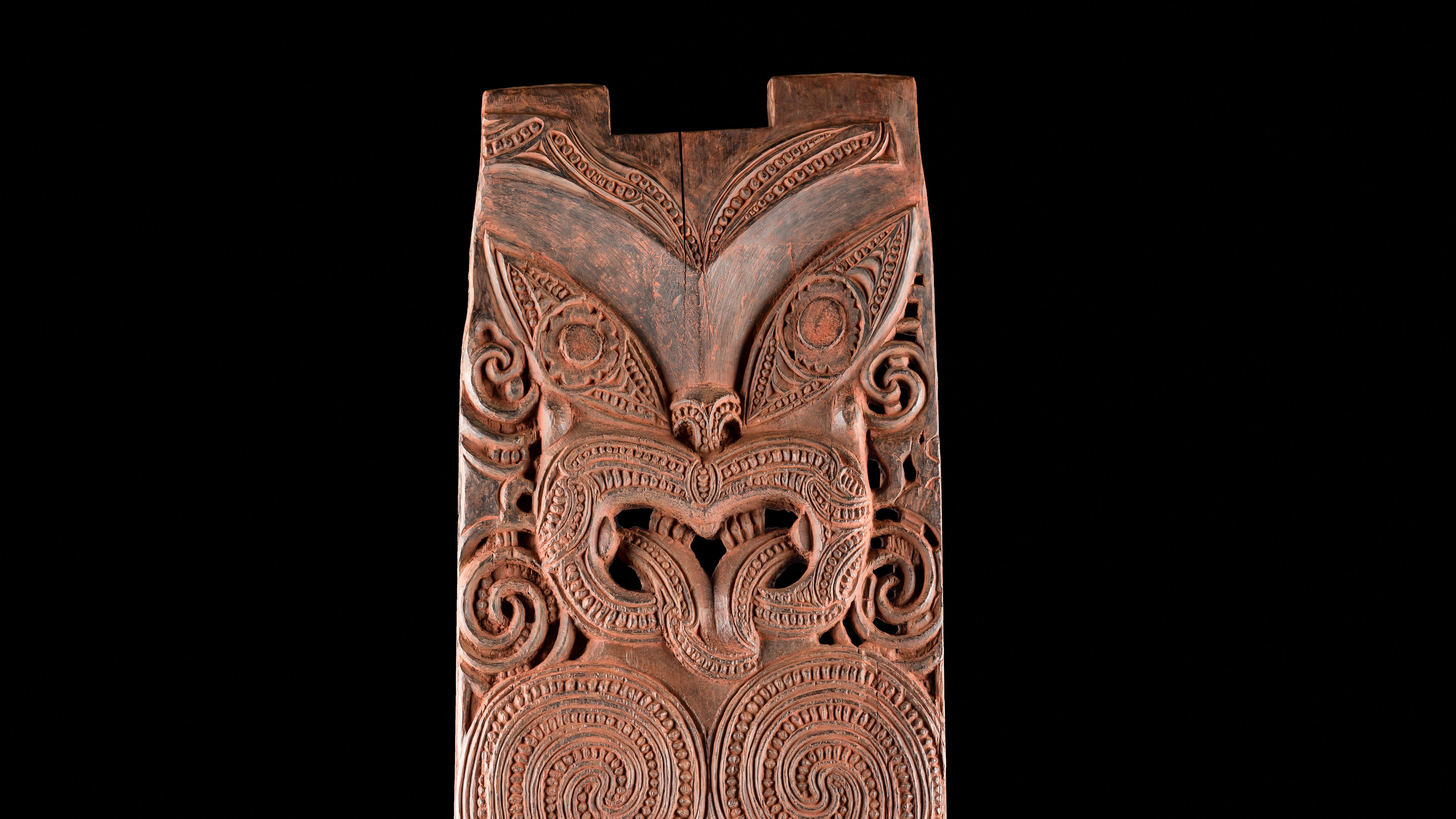 A wooden panel, painted red, depicting a stilised female ancestor, stretching out her tongue