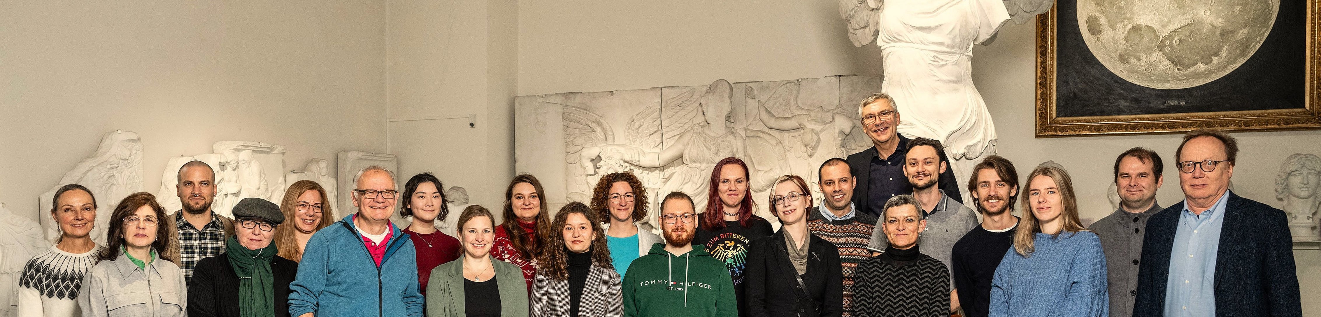 Gruppenfoto des MUT-Teams im Halbrund vor dem Abguss der Nike von Samothrake und dem Mond-Gemälde im Rittersaal