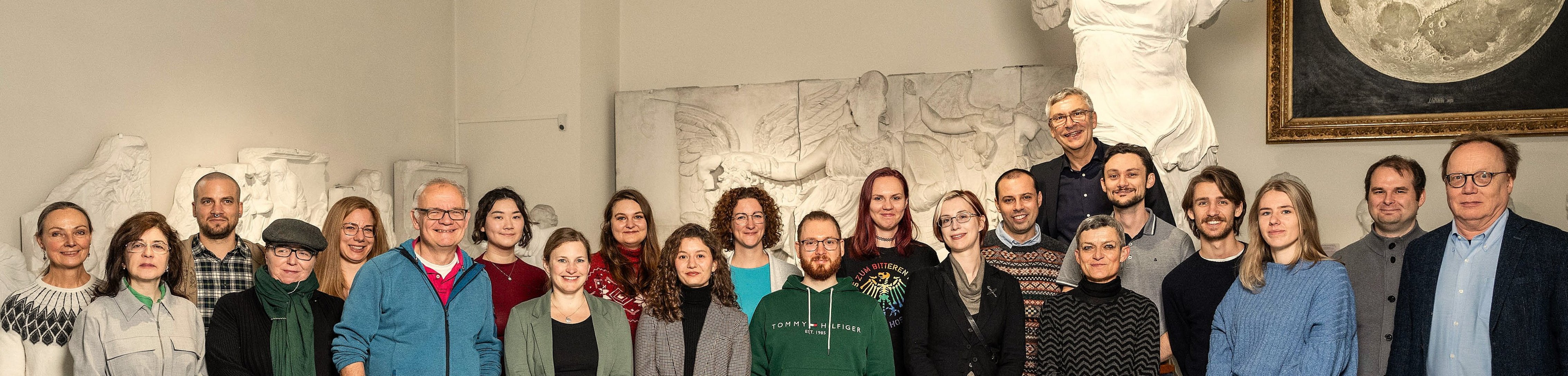 Group photo of MUT employees in a half-circle in front of the plaster cast of Nike of Samothrake in the Knights' Hall of Hohentübingen Castle