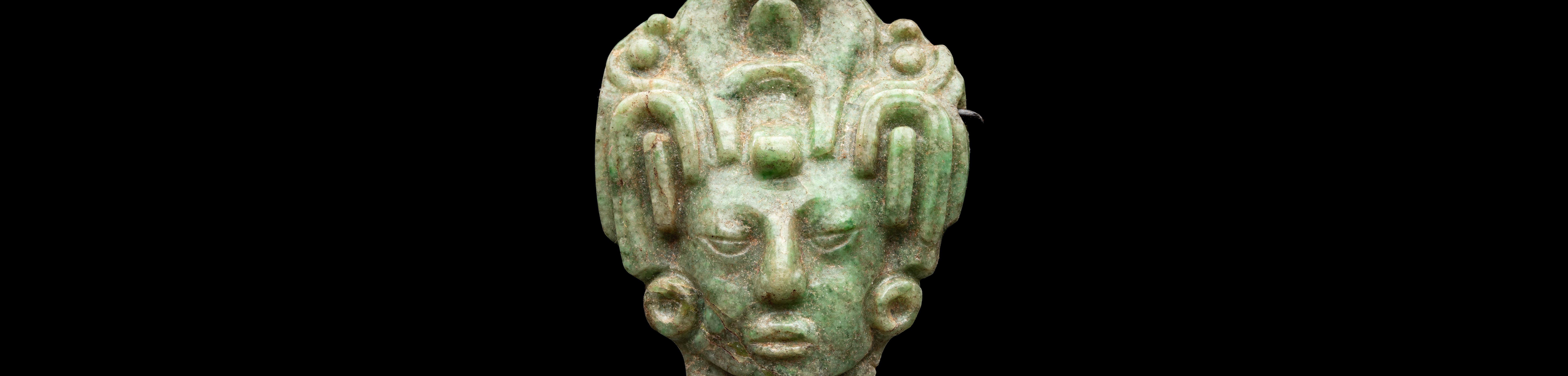 Central green jade head of a maize god against black background