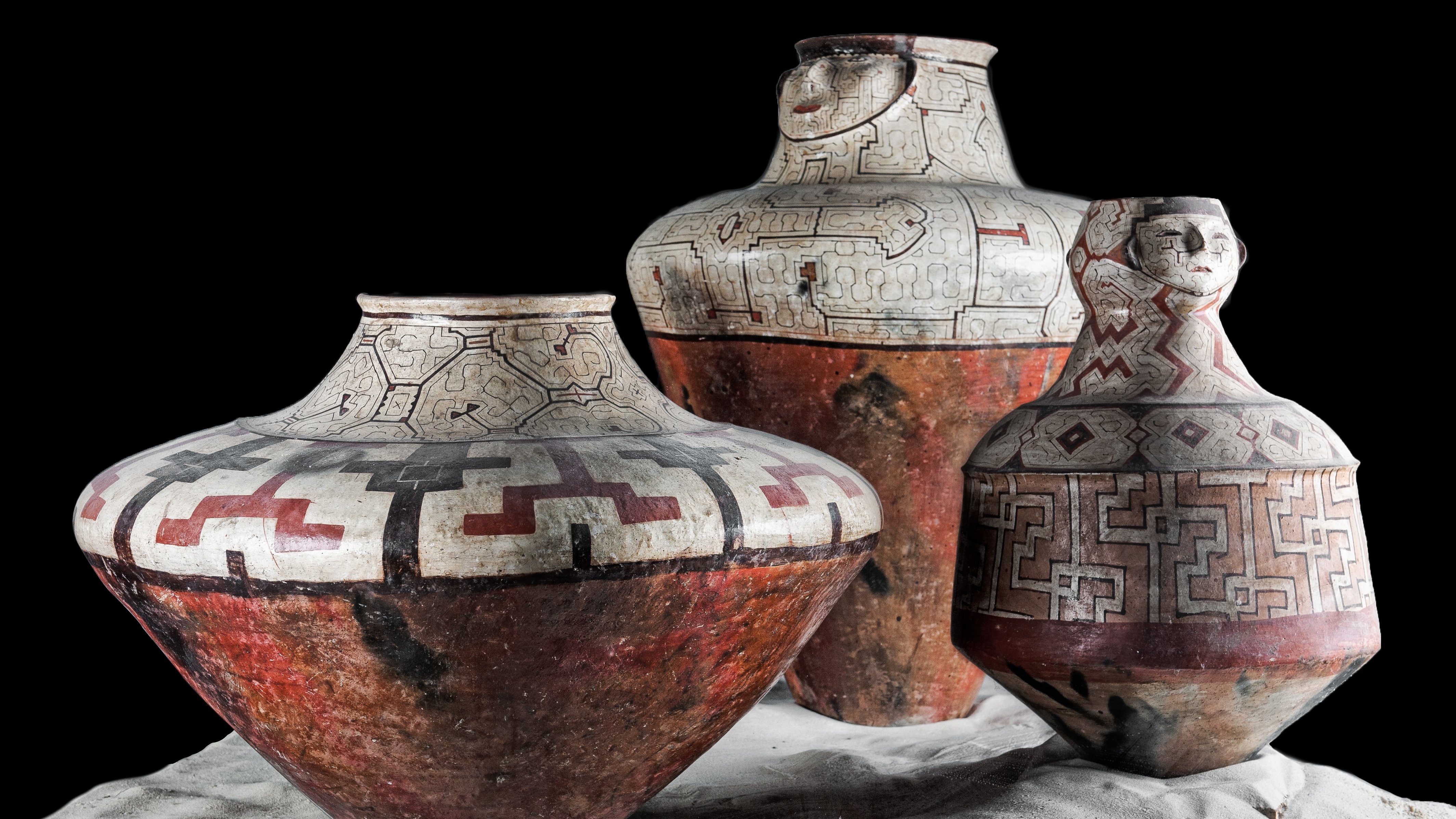 Wide ceramic vessels with black, dark red and blue geometric patterns on white and terracotta background; objects against black background