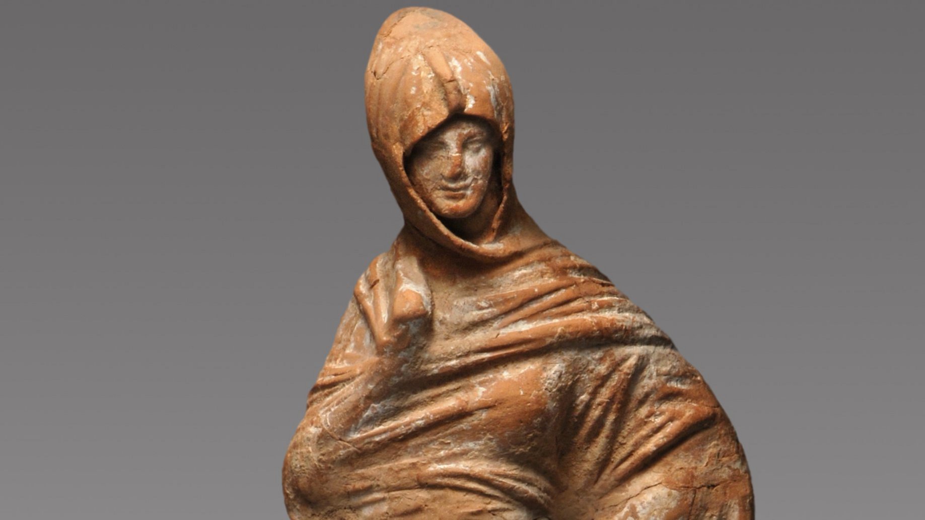 Terrakotta-Statuette einer in ihren Mantel gehüllten Frau, die eine Hand in die Hüfte stemmt und die andere in ihrem Mantel verbirgt