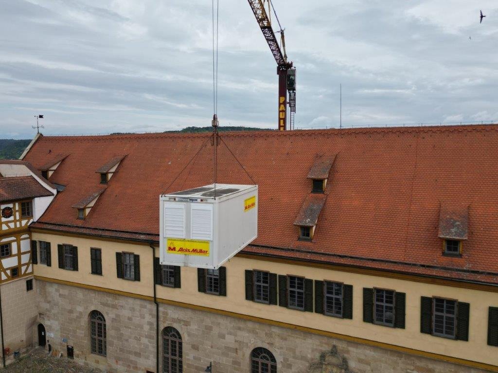 Zu sehen ist ein Kran, der eine Kiste mit Material über das Dach von Schloss Hohentübingen hebt