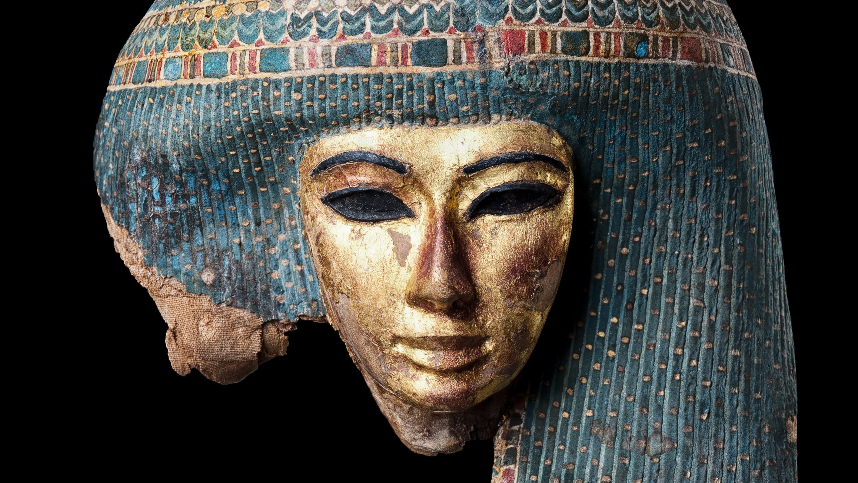 Coloured Egyptian mummy mask with elaborately decorated pearl hairstyle against black background