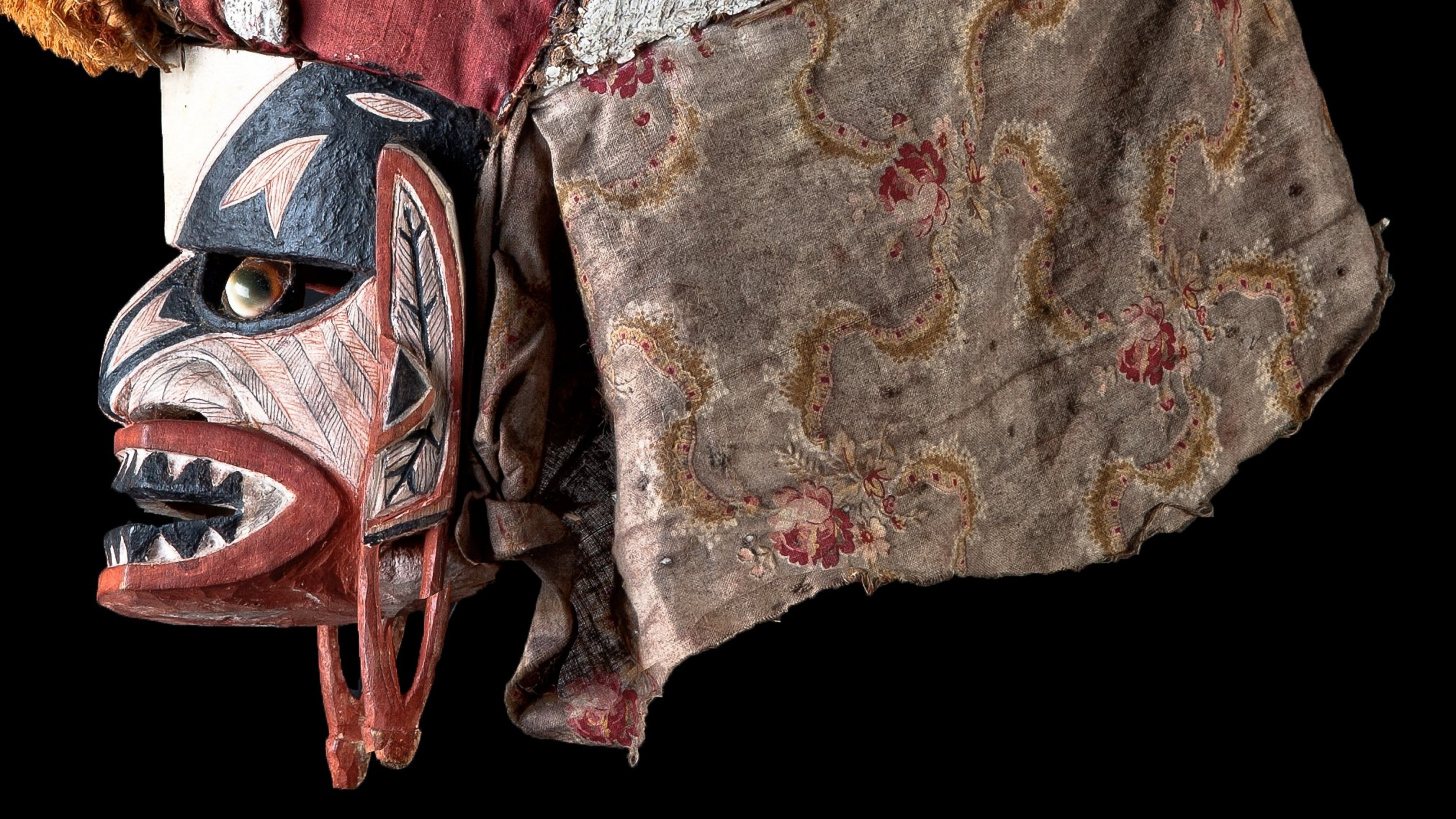 Left-facing, painted mask with open mouth; the mask covers the whole head with patterned fabric covering the neck area