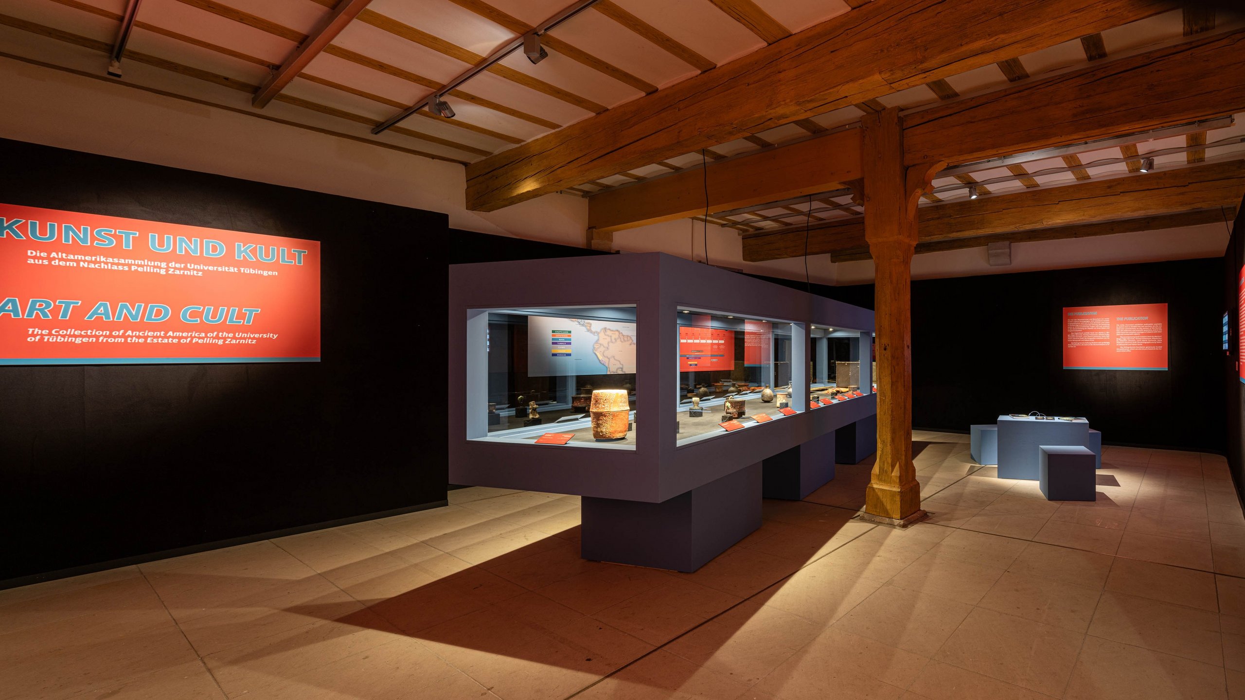 Panorama view of the deserted exhibition with the central, Mayan-blue showcase and illuminated exhibition panels at the black walls