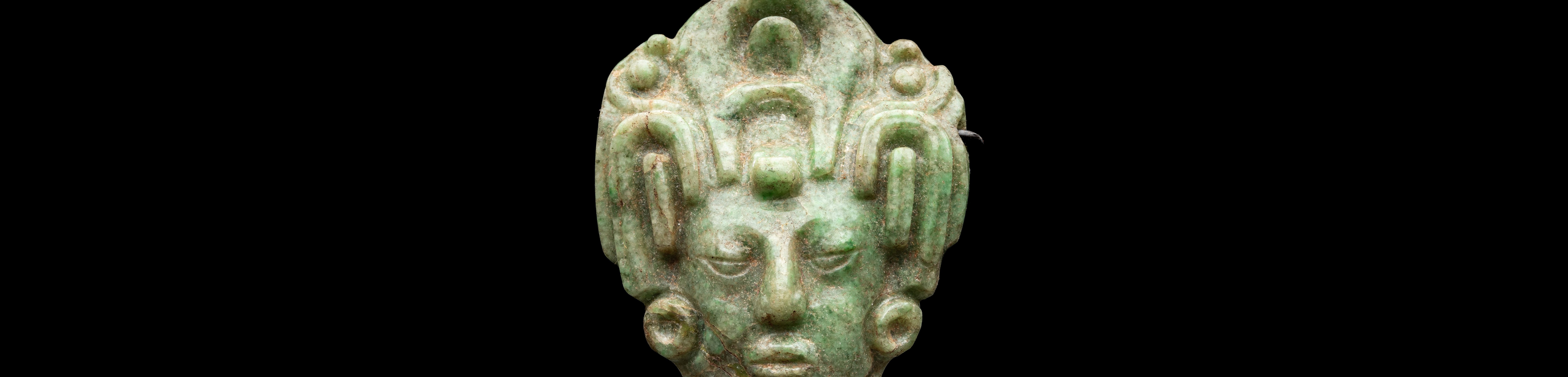 Ein grüner Jadekopf eines Maisgottes der Maya mit Kopfschmuck vor schwarzem Hintergrund