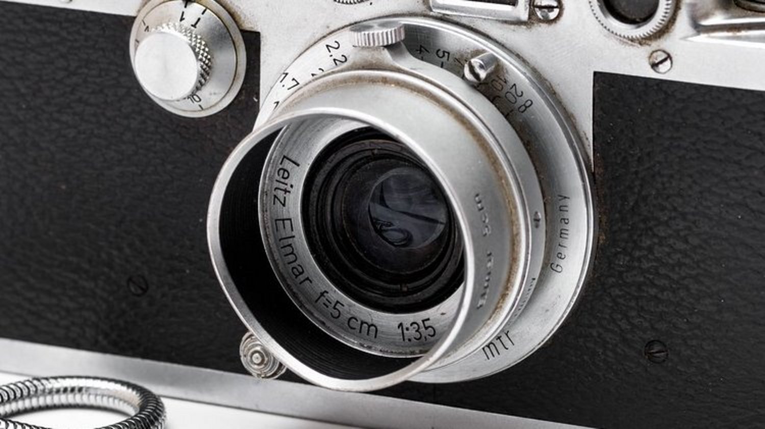 An old camera with a black leather grip and a metal cord to hold it